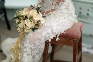 Bride in a luxury bridal dress sitting on a vintage chair and holding her bridal bouquet elegantly